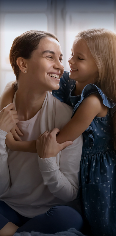 A mother and daughter smiling with arms wrapped around one another.